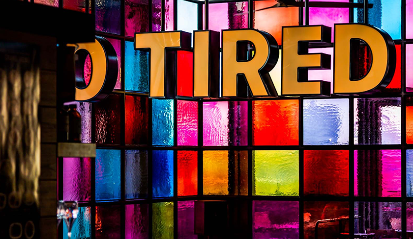 The word "tired" in all caps on a colorful stained glass mosaic background
