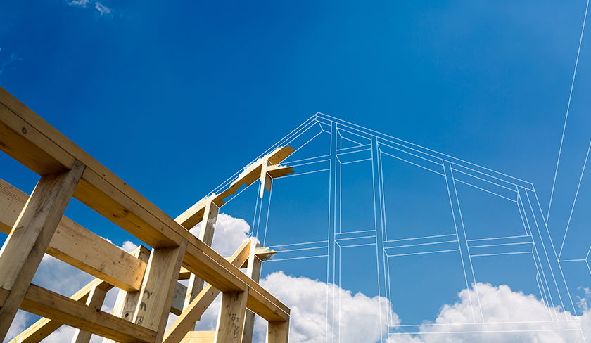The wooden frame of a house being built onto a blueprint with a blue sky in the background